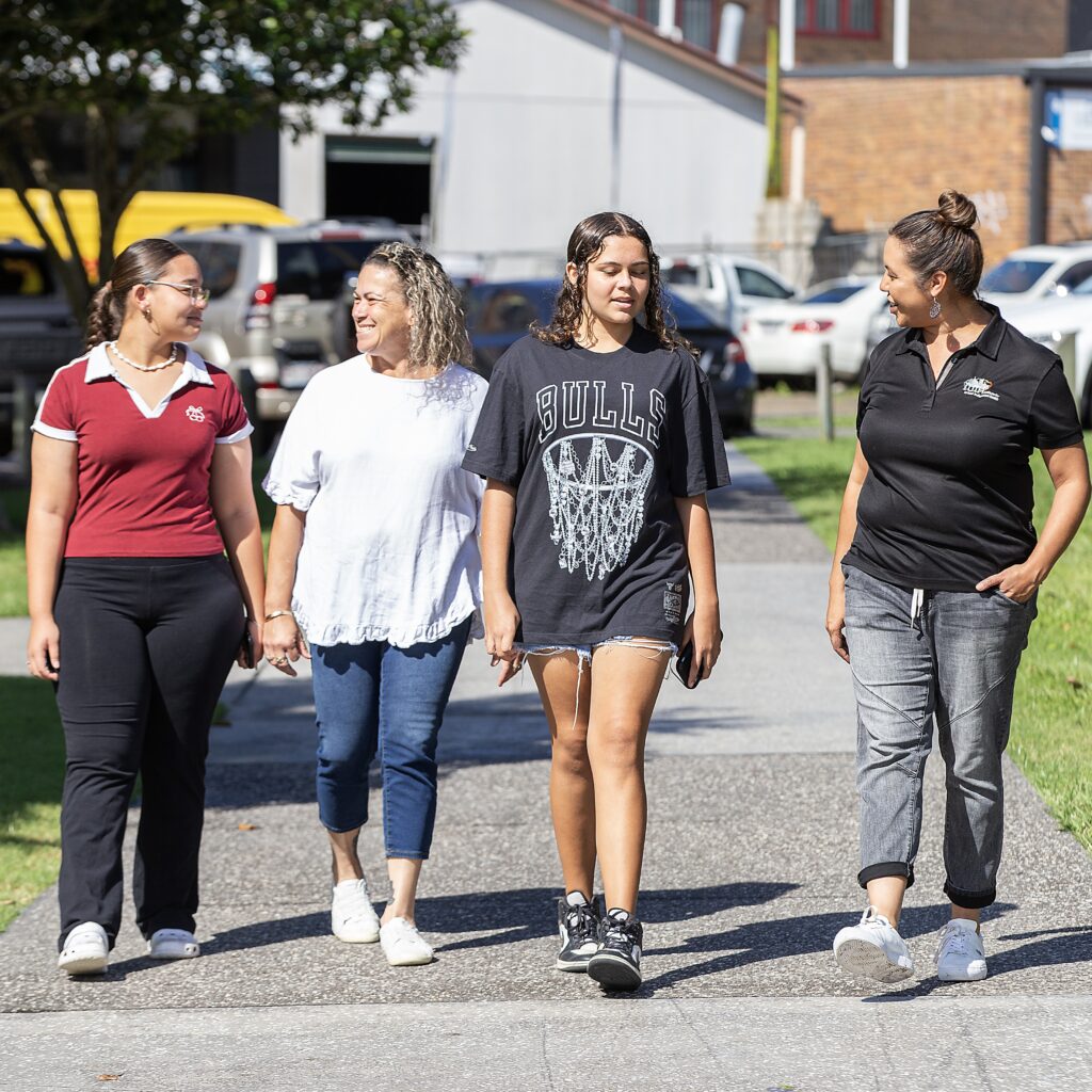 Two women walk alongside two youth, talking and laughing.