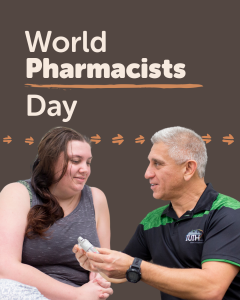 World Pharmacists Day. A pharmacist in a black and green shirt is showing a medical device to another person.