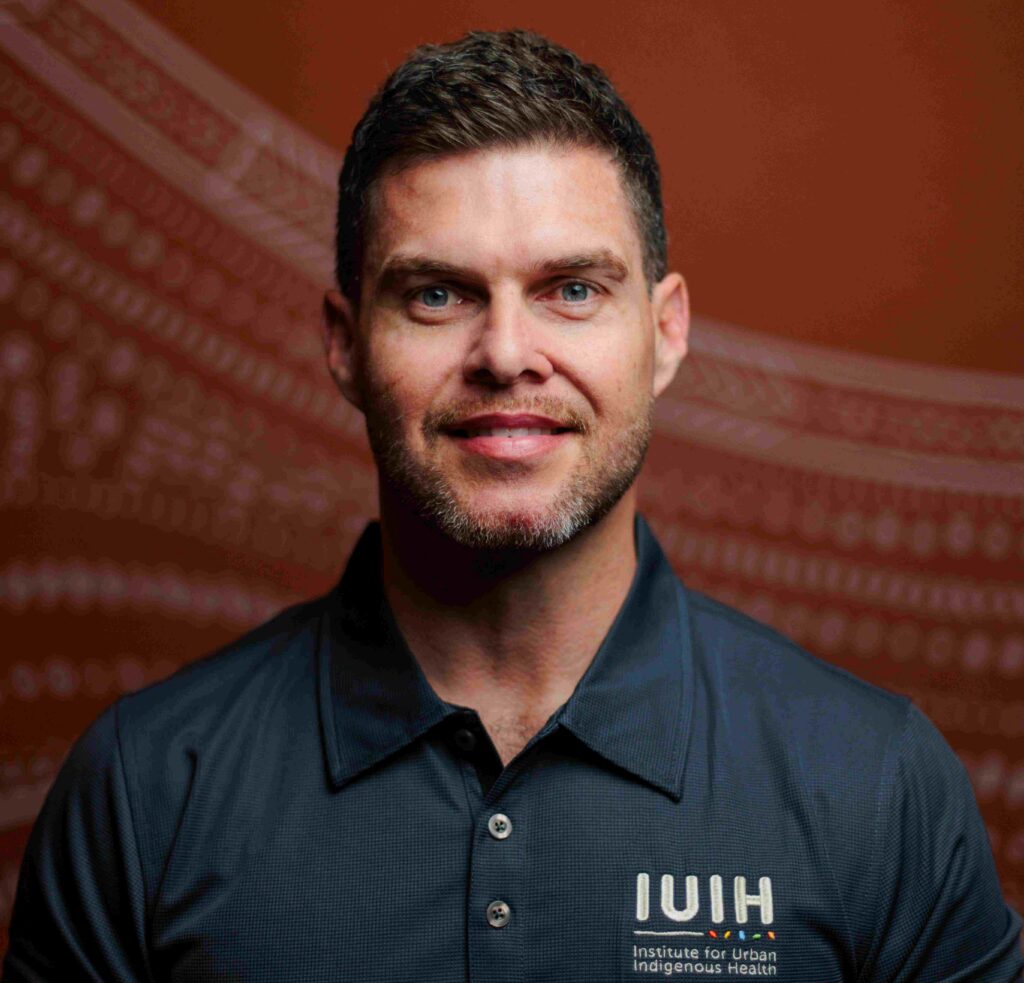 Corey Kirk- man smiling and wearing the IUIH uniform against brick red background.