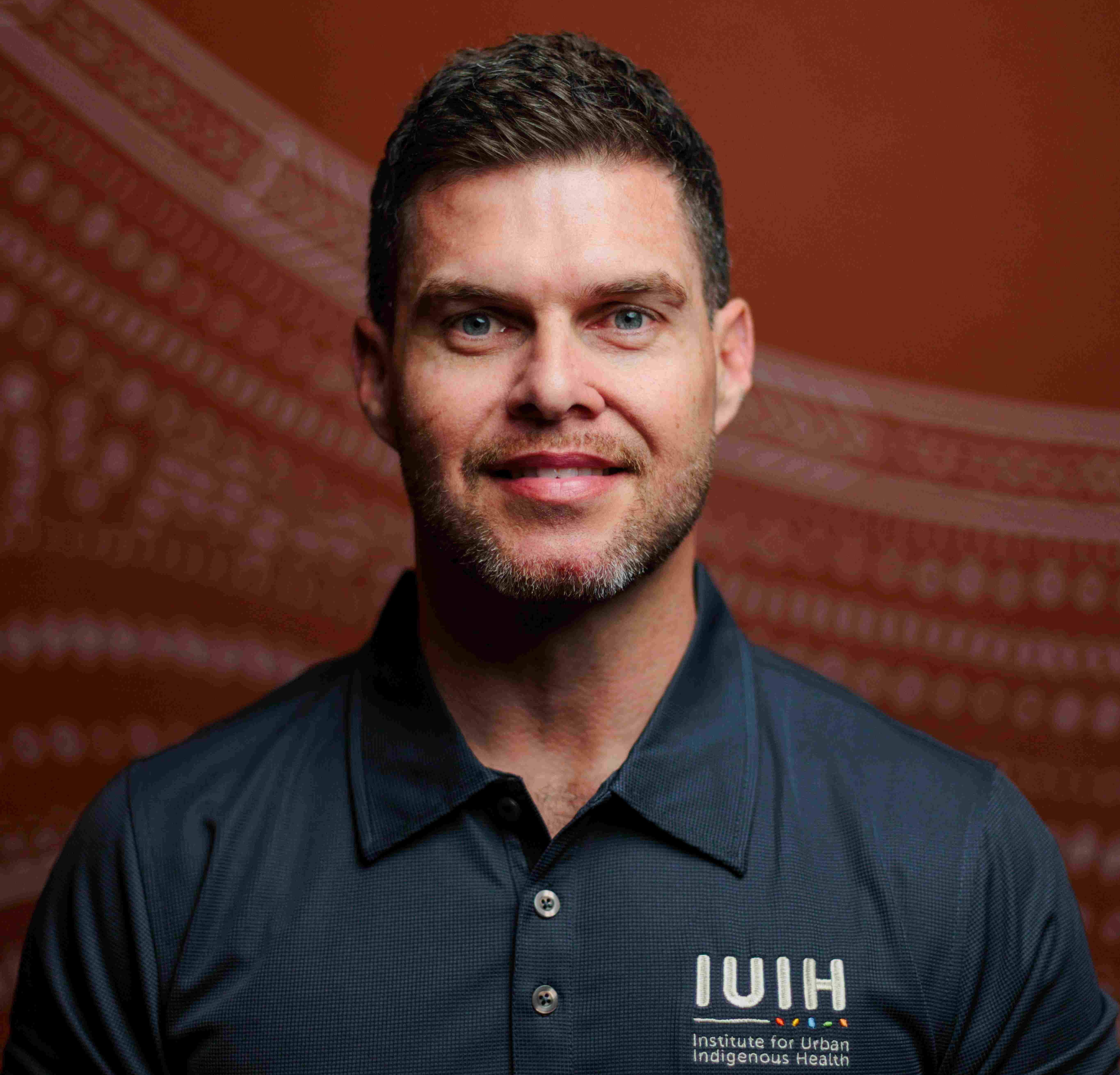 Corey Kirk- man smiling and wearing the IUIH uniform against brick red background.