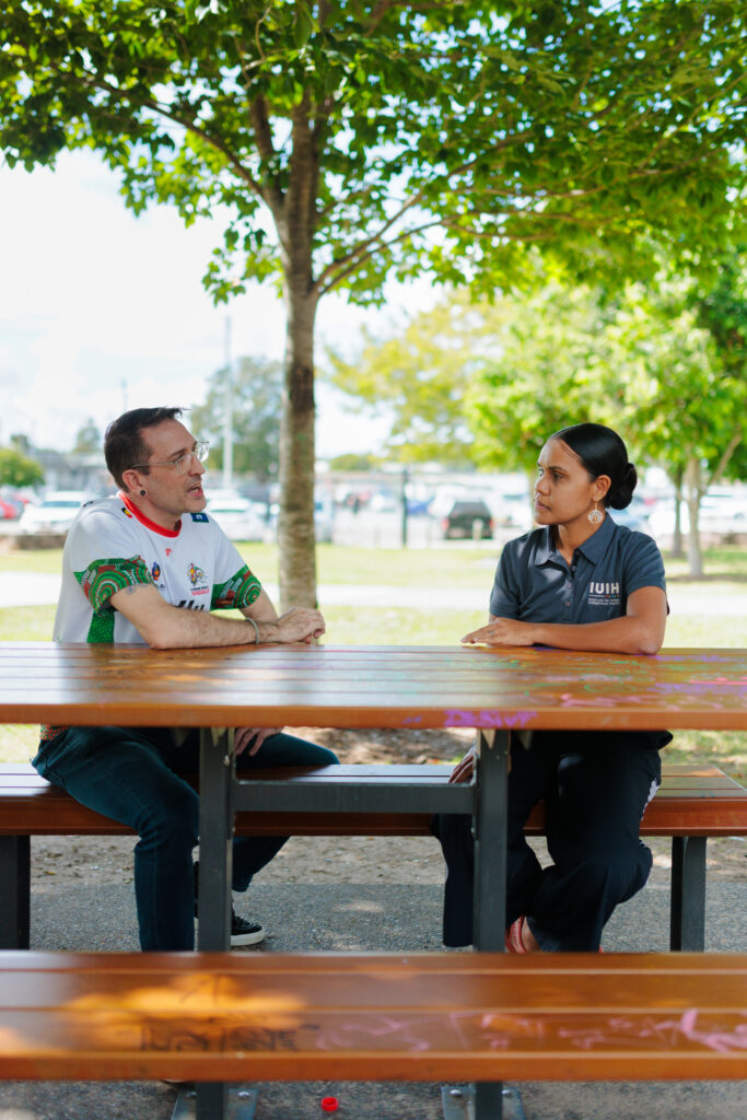 A man and woman who work in community controlled health sit together at a table in a park.