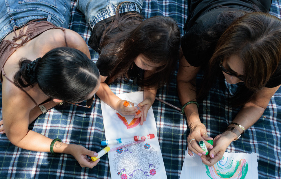 Indigenous allied health team member with clients, colouring in on a picnic rug.