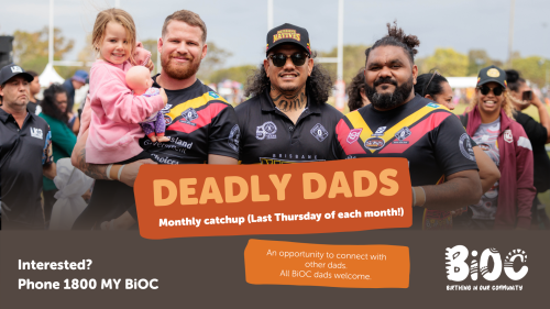 Three men in footy gear and one holding a jarjum.